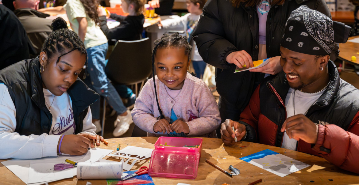 A family of three particpatingn in a family friendly crafty workshop at a busy event.