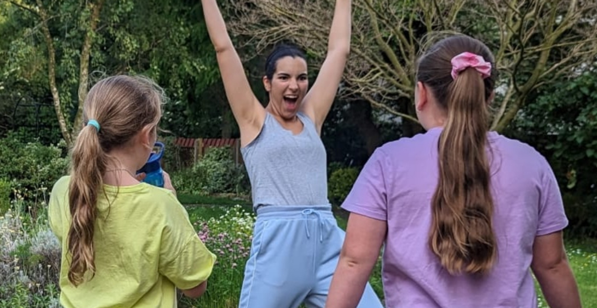 A person engaging two young girls in an active workshop outdoors in a park setting.