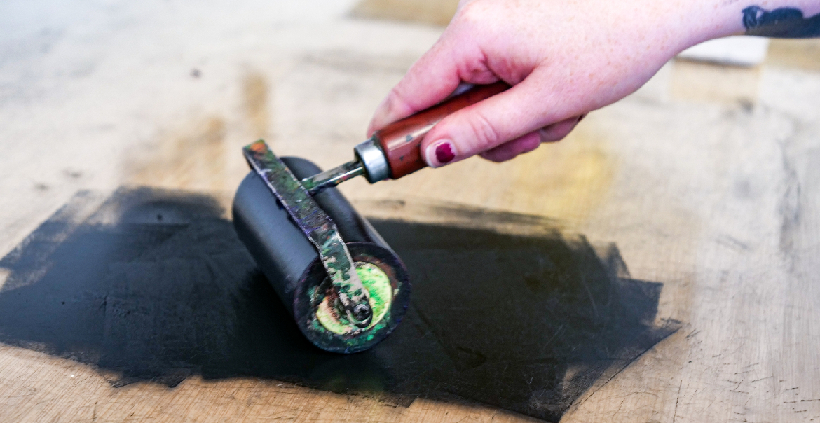 A hand rolling black ink onto a surface.