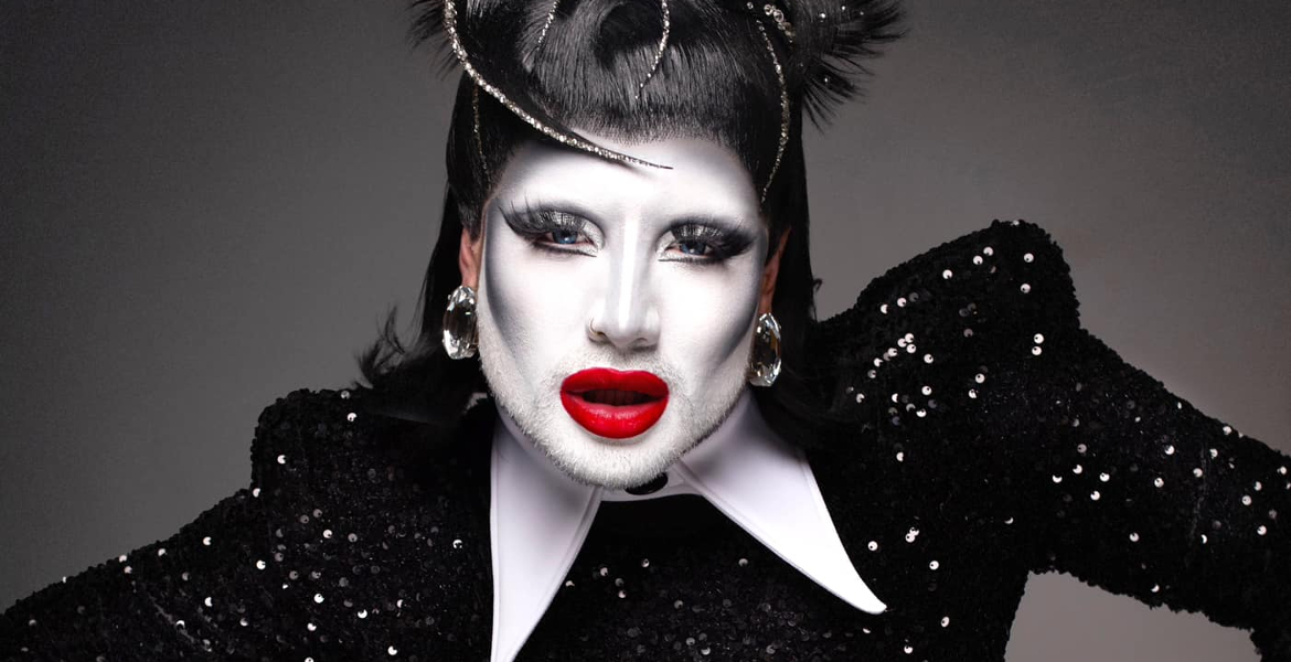 A close-up image of a drag queen wearing white make-up and red lips.