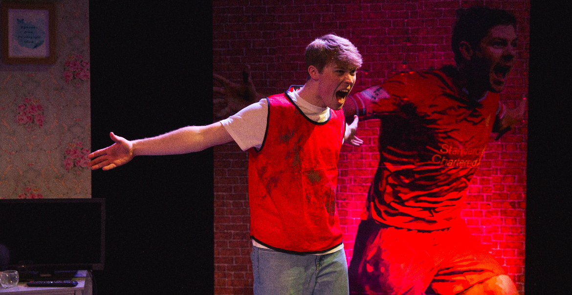 A performer on stage imitating a large mural of Stephen Gerrard behind him.