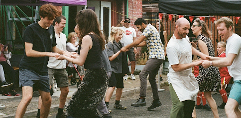 A cheerful crowd of dancers fills the street, moving rhythmically and celebrating together in a festive atmosphere.