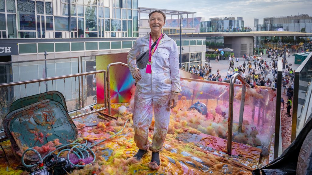 Stood on a balcony, a woman proudly displays a bunch of bright paint, embodying creativity and inspiration in her surroundings.