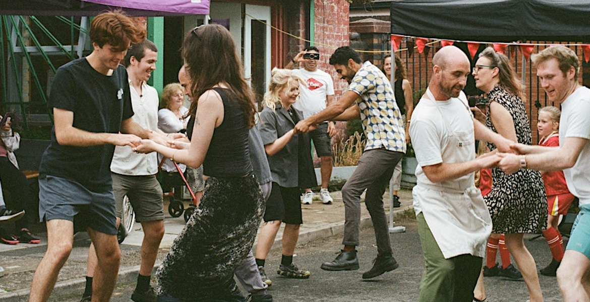 A cheerful crowd of dancers fills the street, moving rhythmically and celebrating together in a festive atmosphere.