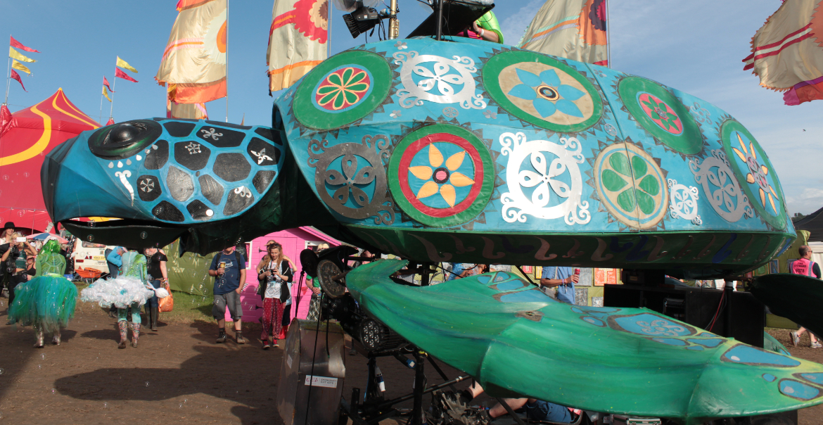 A giant turtule puppet wuith colourful deigns on the shell, at an outdoor event.