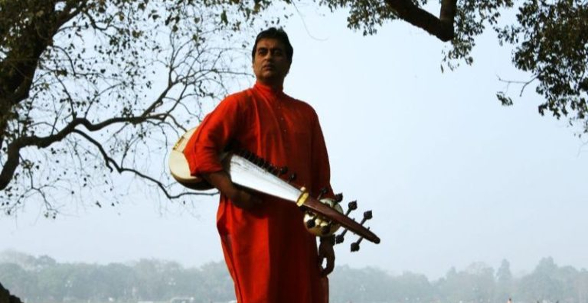 A person with an instrument standing under a tree.