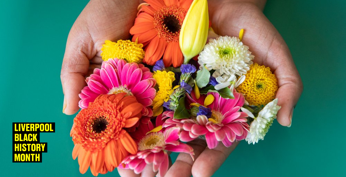 Two hands holding a colorful assortment of fresh flowers including orange gerberas, yellow daisies, and other mixed blooms against a teal background.