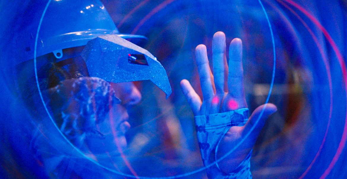 Person in a helmet with a visor examining holographic displays emanating from their hand.