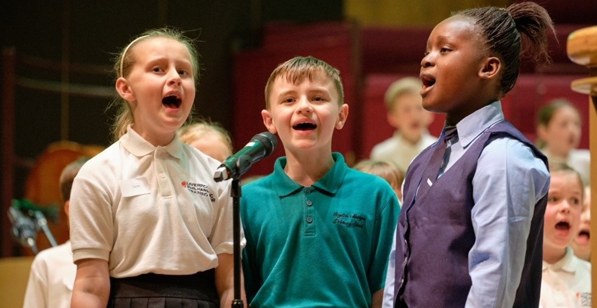 Three children singing on stage into a mic.