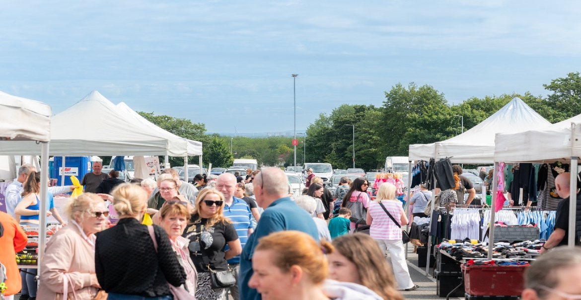 An image of an ourdoor market with lots of shoppers under a blue sky.