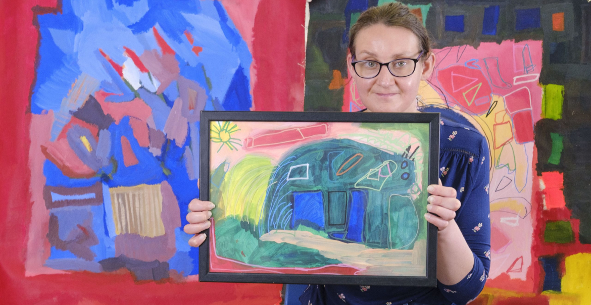 An image of a woman holding up a colourful painting with lots of shapes.