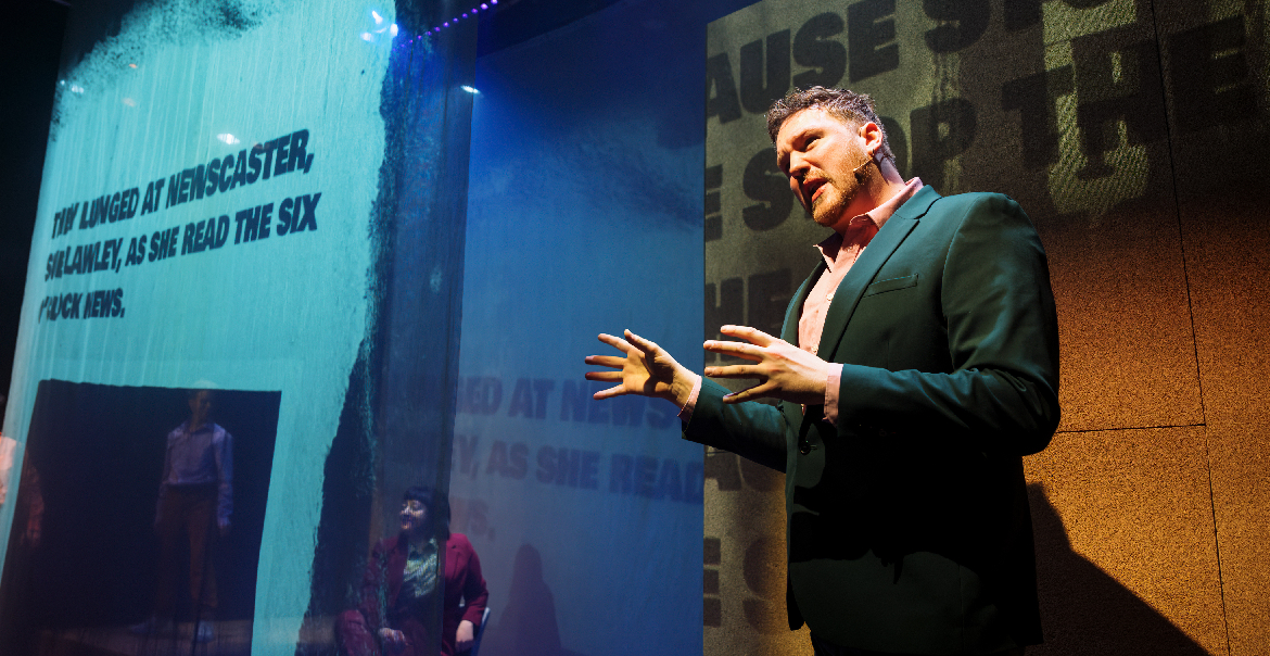 A production image of an actor on stage with projected words behind him